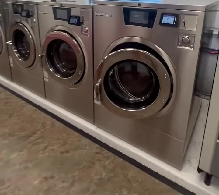 A row of stainless-steel front-load washers, each with its own card reader and coin slot